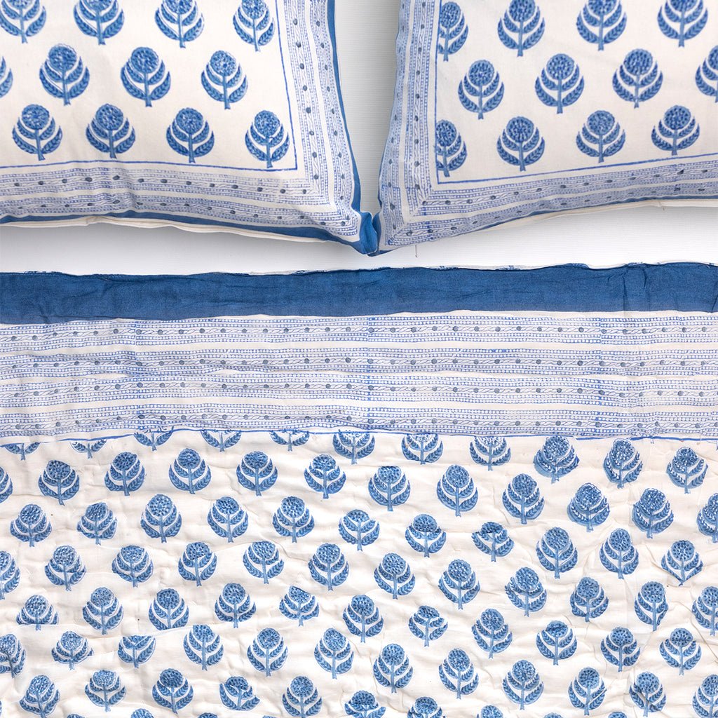 Blue and white patterned quilt and pillows on a white background