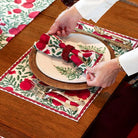 Person setting a festive table with red and green patterned napkins and placemats.
