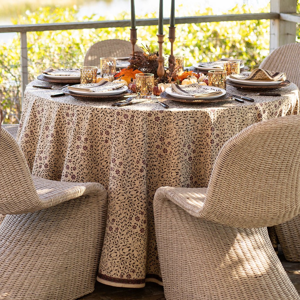 Dining table set for a meal with a patterned tablecloth and chairs outdoors.