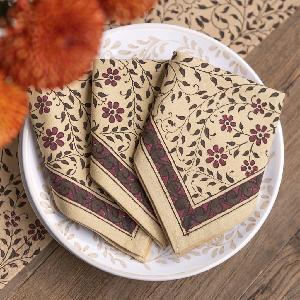 Three napkins with floral patterns on a white plate on a wooden surface.
