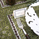 Green patterned tablecloth with a fork, knife, and name card on a decorative setting.