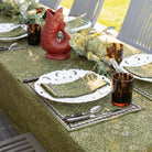 Dining table setting with green tablecloth, white plates, and amber glasses.