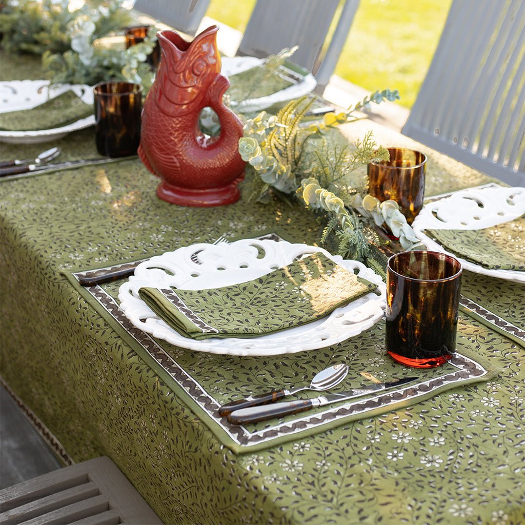 Table setting with green patterned placemat, napkin, and tablecloth.