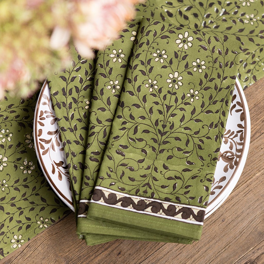 Green patterned napkins on a wooden table with floral elements.