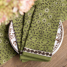 Green patterned napkins on a wooden table with floral elements.