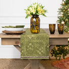 Decorative table setting with a green table runner, vase with flowers, and candles on a wooden table.