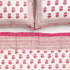 Pink and white patterned quilt and pillow set on a white background