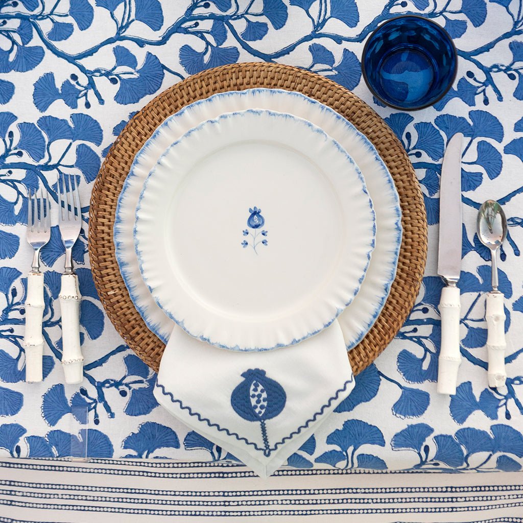 Dining table setting with white plates, blue floral patterns, and wicker charger on a blue and white floral tablecloth.