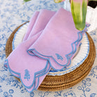 Pink napkin with blue trim on a stack of plates with a floral tablecloth background