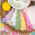 Colorful scalloped cocktail napkins on a woven mat with a lemon and floral plates.