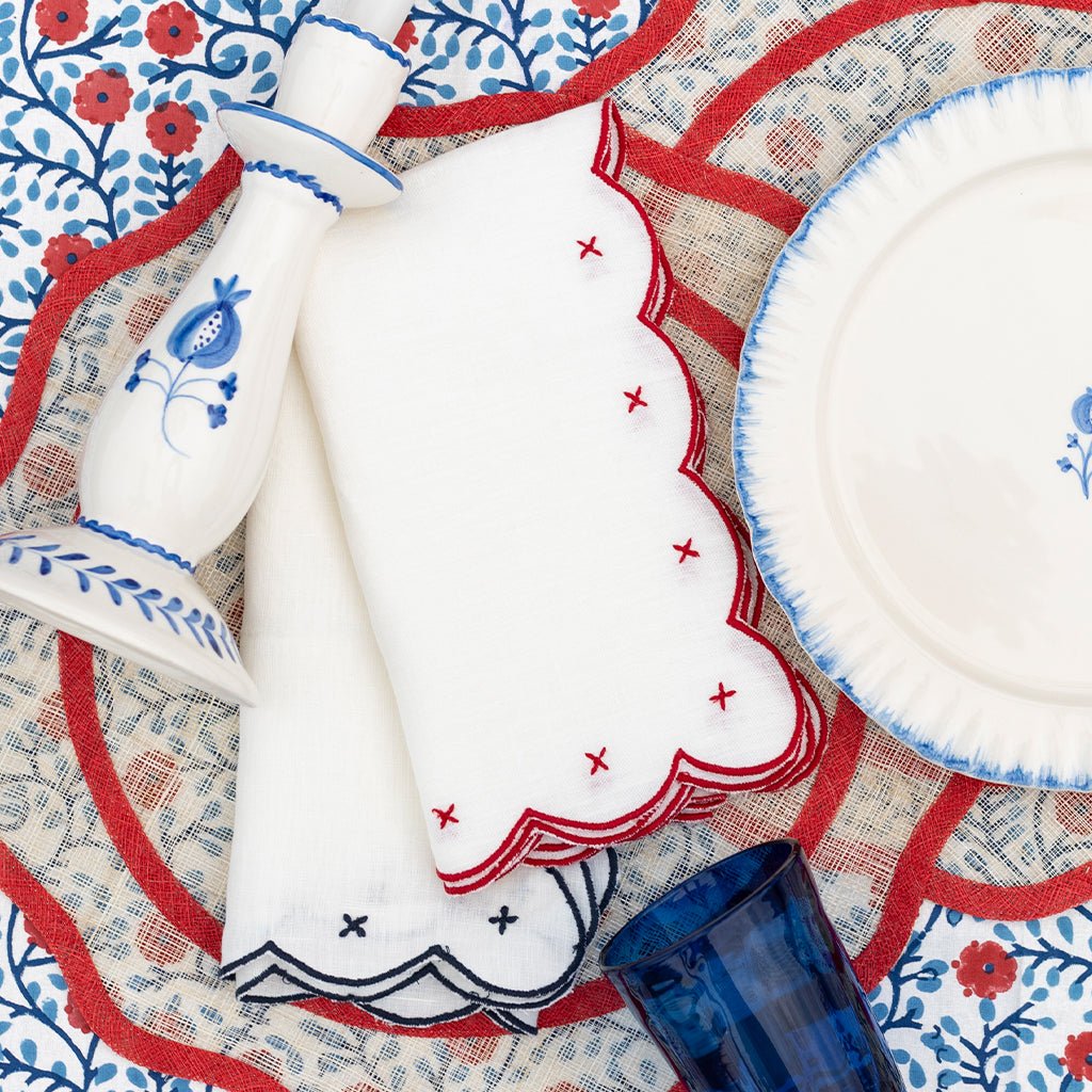 Decorative table setting with white plates, blue and red patterned placemats, candlestick, and a blue glass.