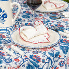 Dining table setting with floral tablecloth, plates, cutlery, and a glass of red wine.