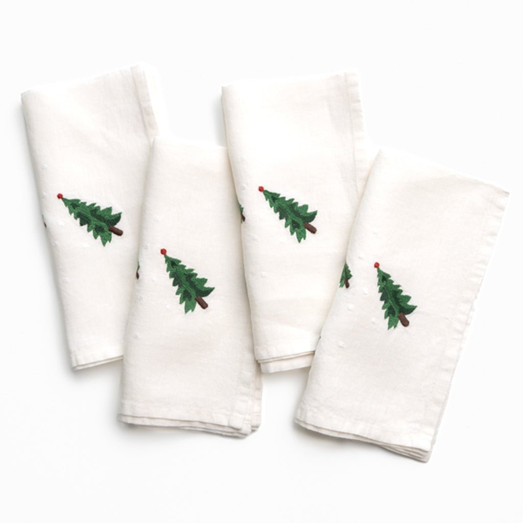Set of four white napkins with embroidered green trees on a white background