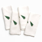 Set of four white napkins with embroidered green trees on a white background
