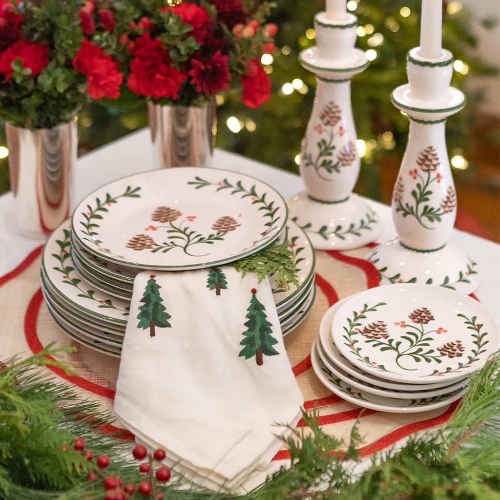 Christmas-themed table setting with decorative plates, napkins, and candles in front of a decorated tree.