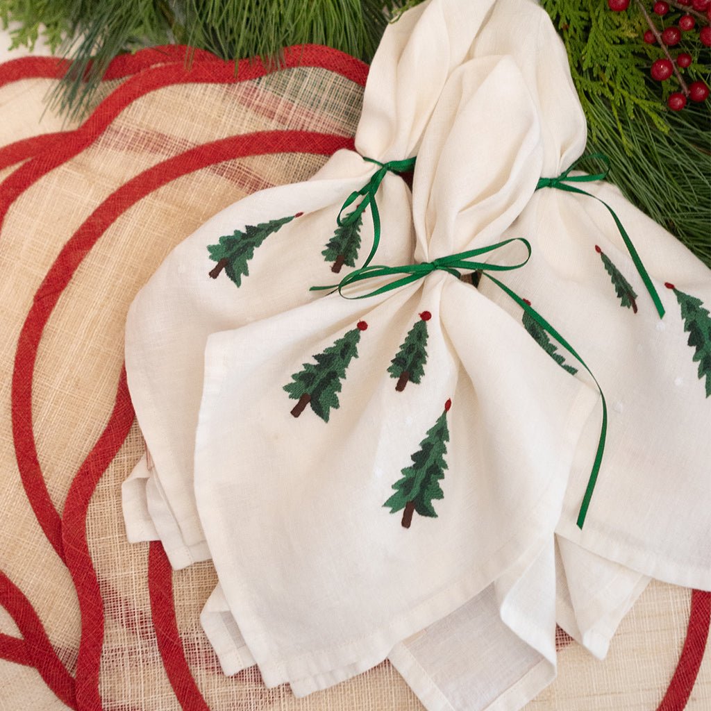 White napkin with embroidered green trees on a red and beige woven placemat.
