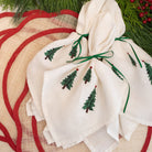 White napkin with embroidered green trees on a red and beige woven placemat.