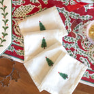 Set of white napkins with Christmas tree designs on a decorative table runner.