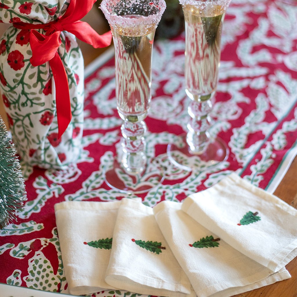Two champagne flutes with decorative glasses on a red and white patterned tablecloth, accompanied by Christmas-themed napkins.