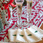 Two champagne flutes with decorative glasses on a red and white patterned tablecloth, accompanied by Christmas-themed napkins.