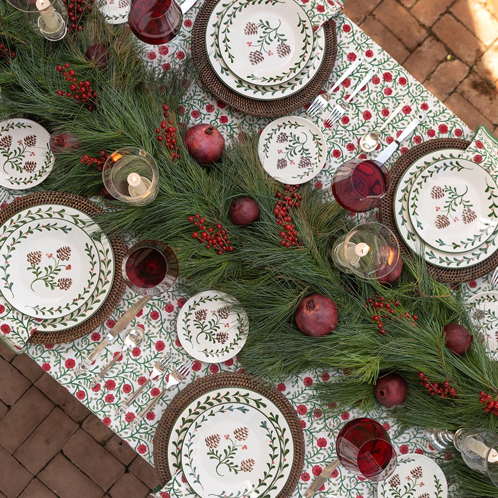 Decorative Christmas table setting with plates, glasses, and greenery on a patterned tablecloth.