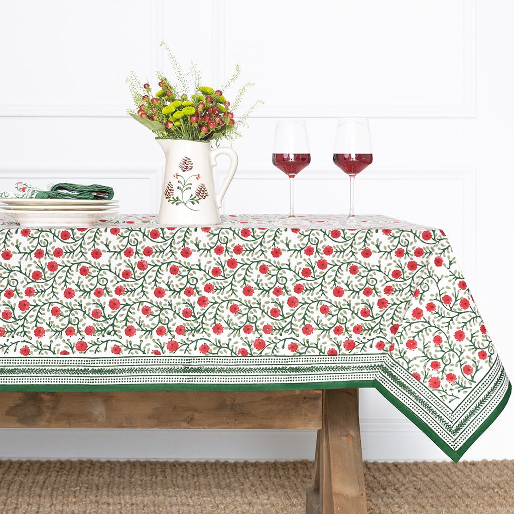 Tablecloth with floral pattern on a wooden table with a vase and glasses.