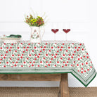Tablecloth with floral pattern on a wooden table with a vase and glasses.