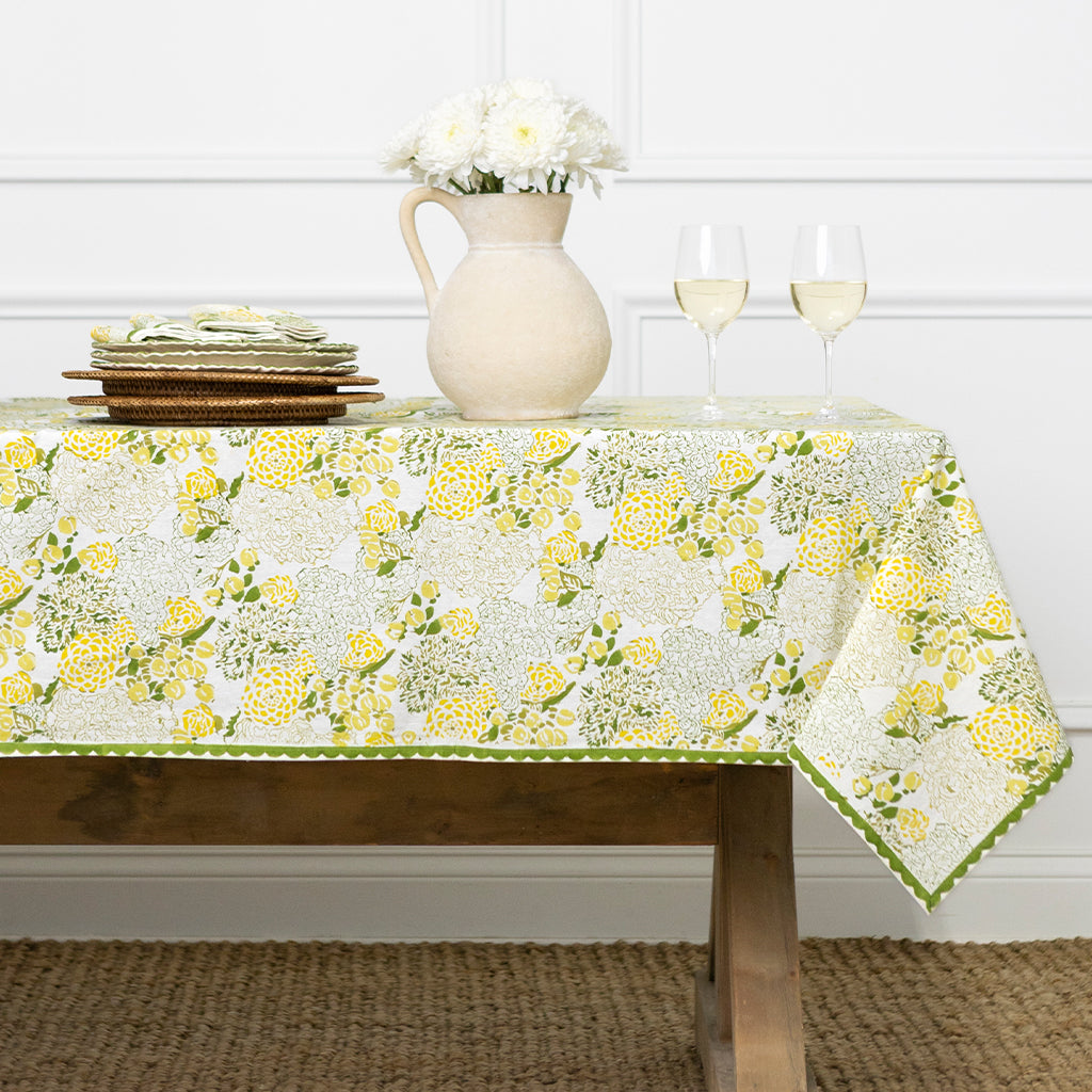 Table with yellow and green floral tablecloth, plates, and glasses on a wooden table.