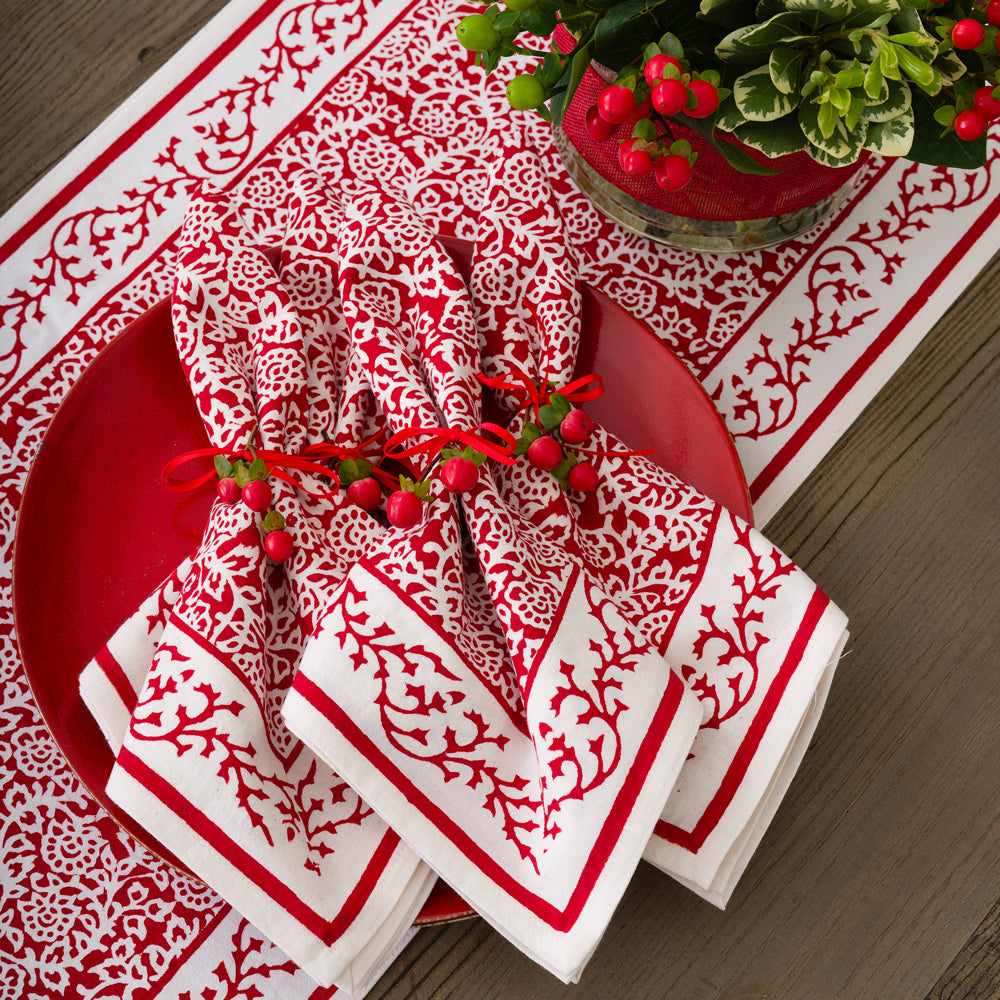 Red and white patterned napkins on a red plate with a decorative plant on a wooden table.
