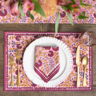 Dining table setting with pink floral placemat, plate, and cutlery on a wooden surface.
