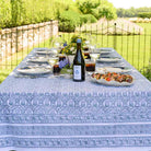 Outdoor dining table set with a blue patterned tablecloth, wine, and food in a garden setting.