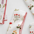 Linen napkin with floral design and red scalloped stitch. 