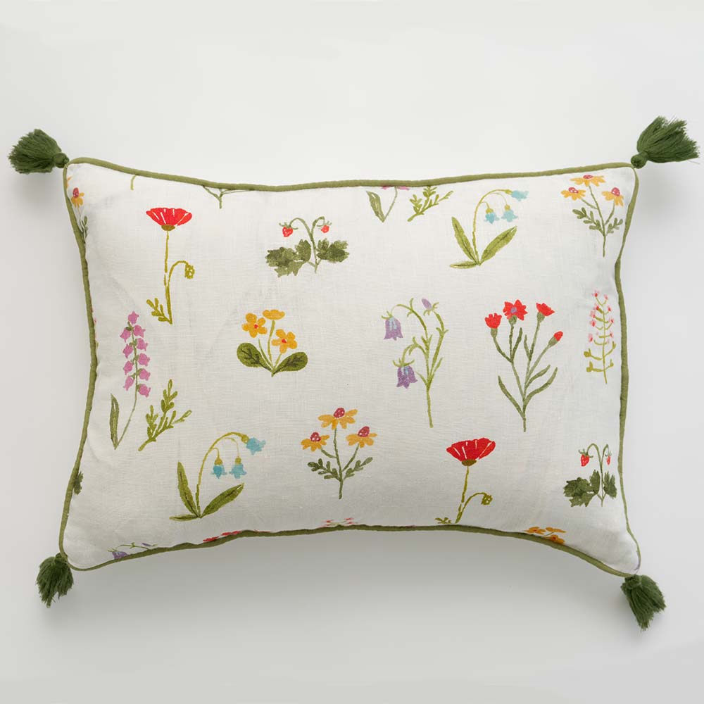 Pillow cover with red poppy flowers, mini yellow daffodils, and lavender bluebells on a soft white linen base with green outline detailing and pom poms. 
