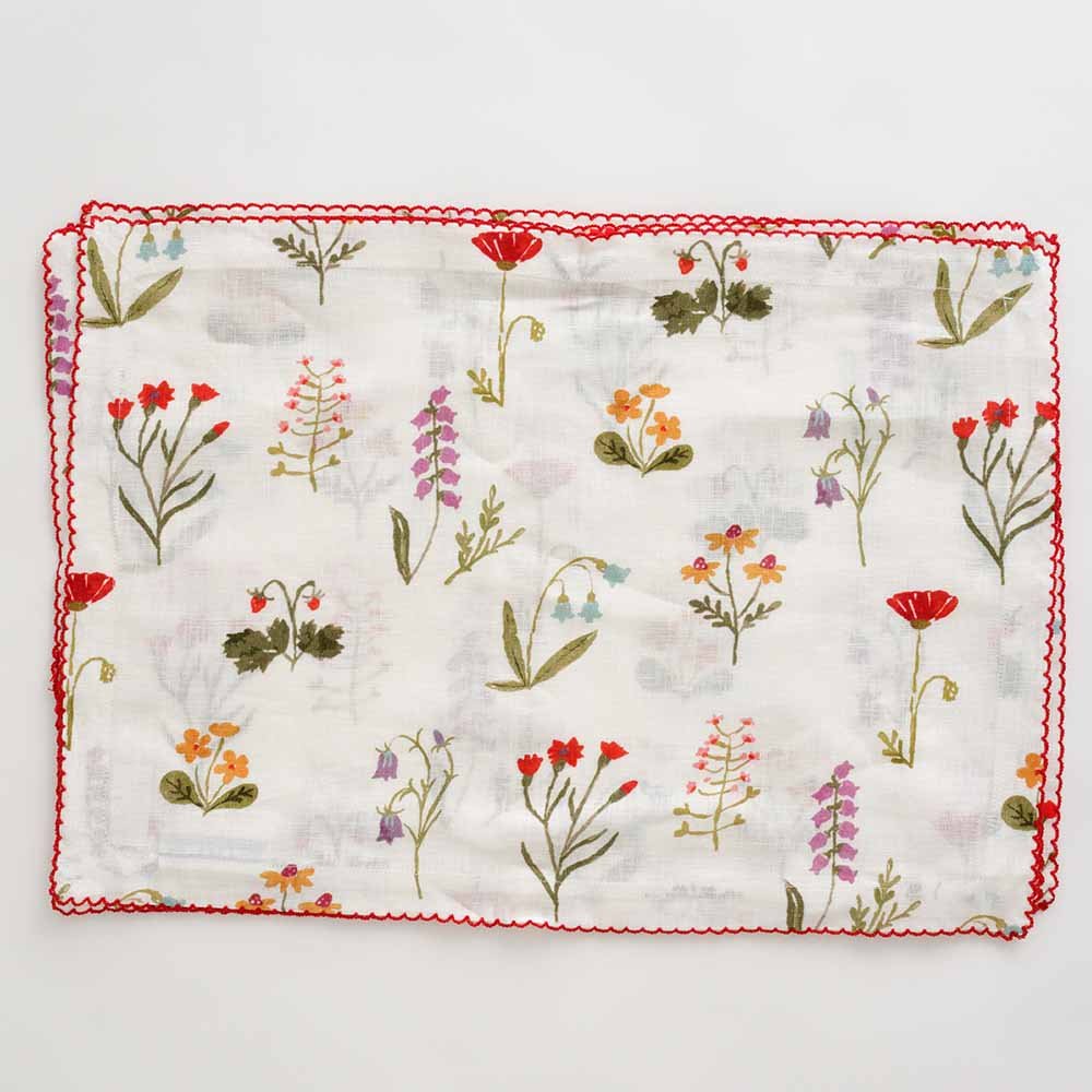 Linen placemat with red poppy flowers, mini yellow daffodils , and lavender bluebells on a soft white linen base with a red scalloped stitch. 