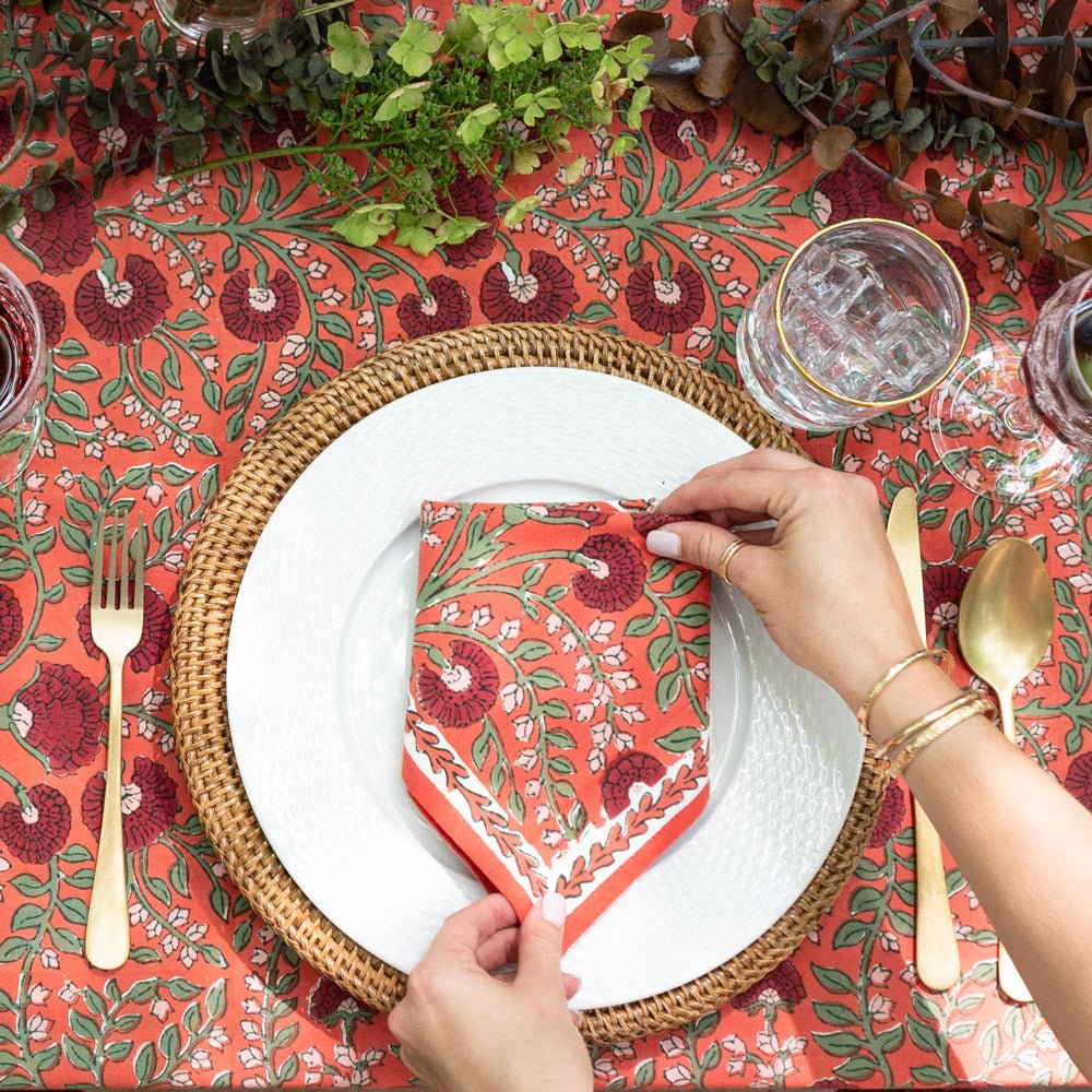 hands placing cactus flower red napkin on white plate with matching tablecloth