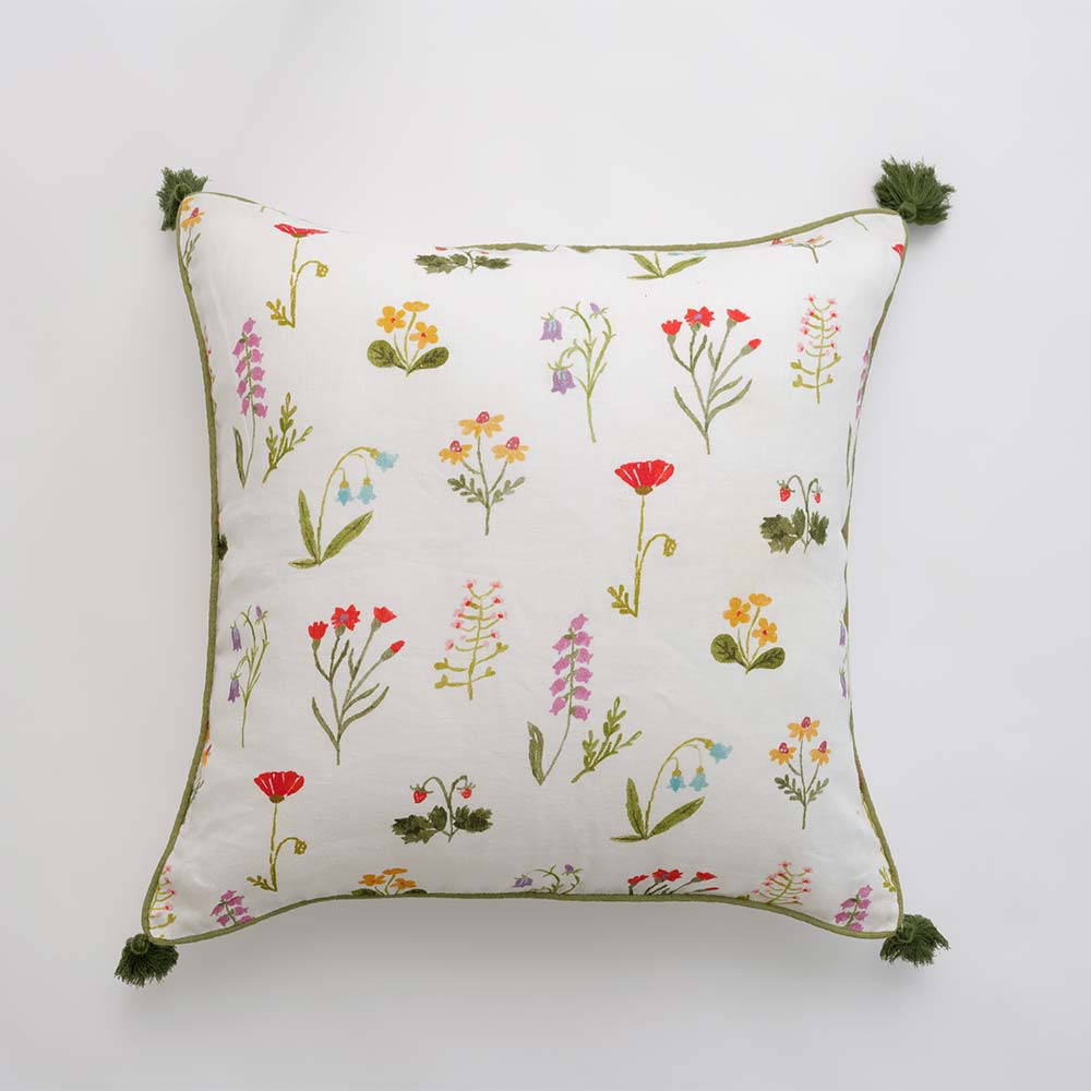 Throw pillow cover with red poppy flowers, mini yellow daffodils, and lavender bluebells on a soft white linen base with green border stitching and pom poms. 