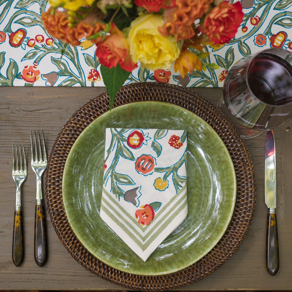 napkin with floral pattern in shades of sage green, crimson, marigold and deep orange laying on a green plate