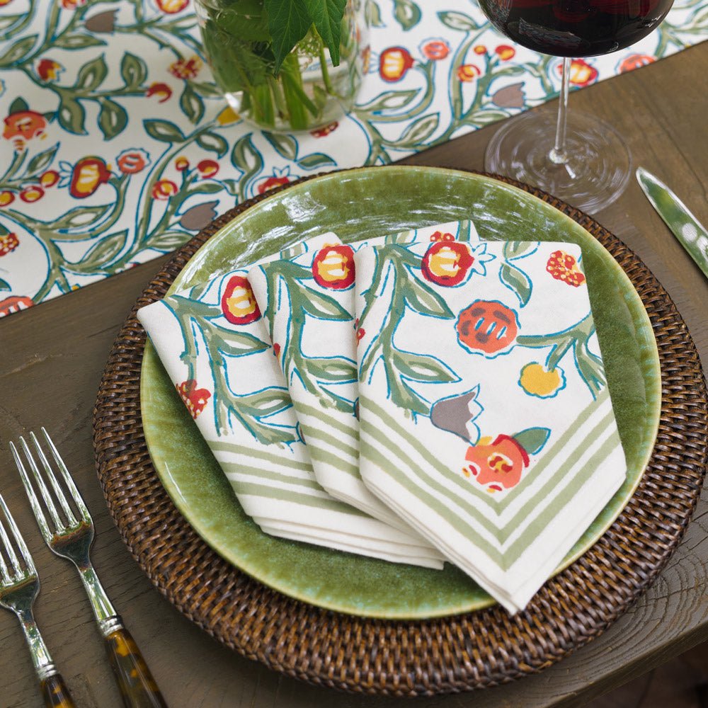 3 napkins with floral pattern in shades of sage green, crimson, marigold and deep orange laying on a green plate