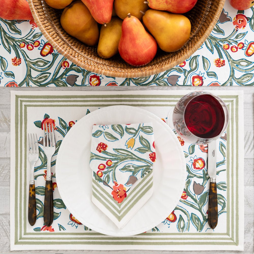 stack of placemats printed with green vines and floral buds in shades of crimson, marigold, and deep orange on white background