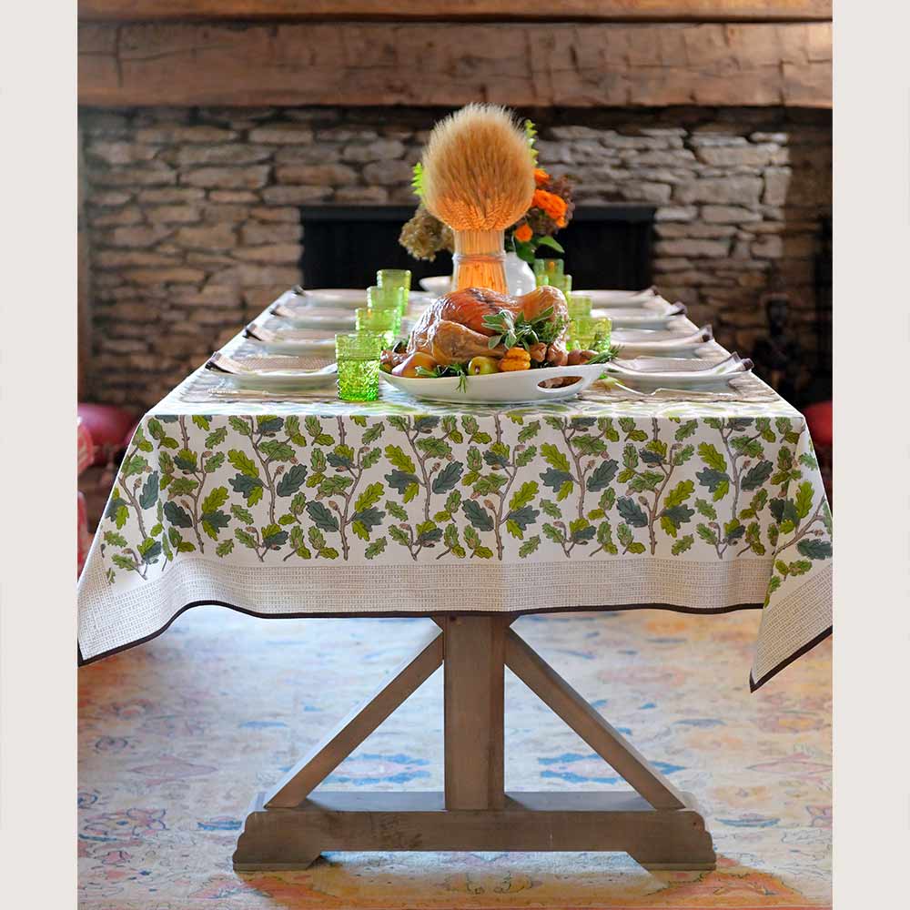 Tablecloth on dinner table with food, plants, and green dishes. 
