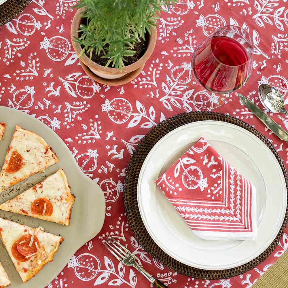 Napkin folded on white plate with matching tablecloth, wine, pizza, and plants. 