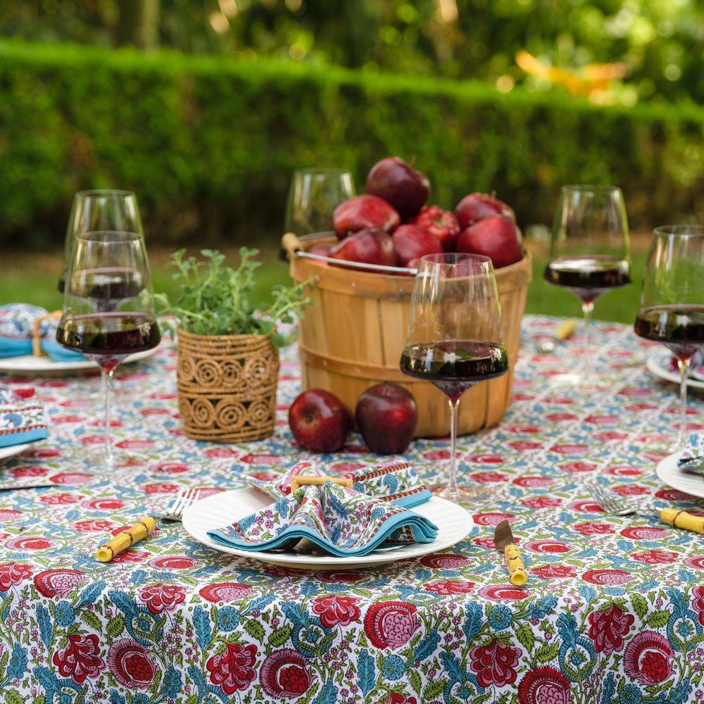 bohemian floral turquoise and cranberry tablecloth on round table outdoors with apples and matching napkins on white plates