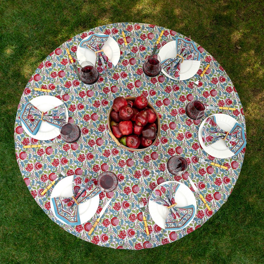 overhead view of bohemian floral turquoise and cranberry tablecloth on round table outdoors with apples and matching napkins on white plates