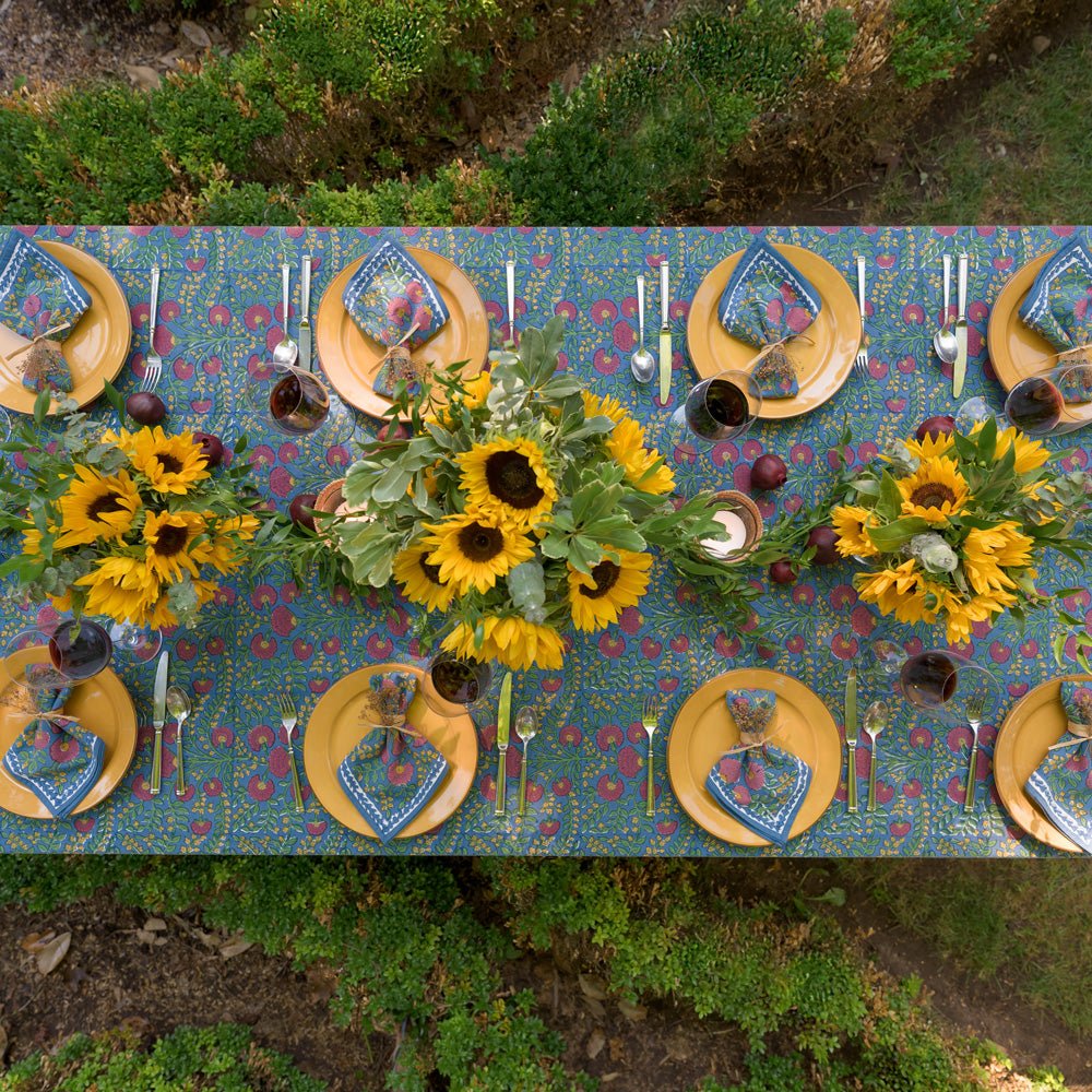 overhead view of Cactus Flower Midnight Dark Blue & Magenta Floral Tablecloth outdoors set with yellow plates and sunflowers and matching napkins