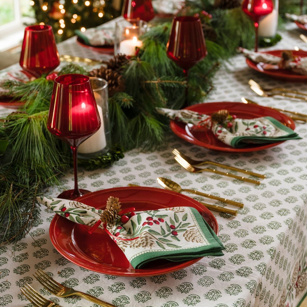 Christmas Garland Table setting with matching napkins and tablecloths on red plates with greenery and pinecones 