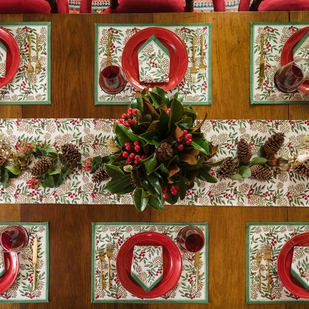 Table Runner with Christmas Garland Print Green Florals & Berries and Pinecones on table with matching placemats, red plates and napkins