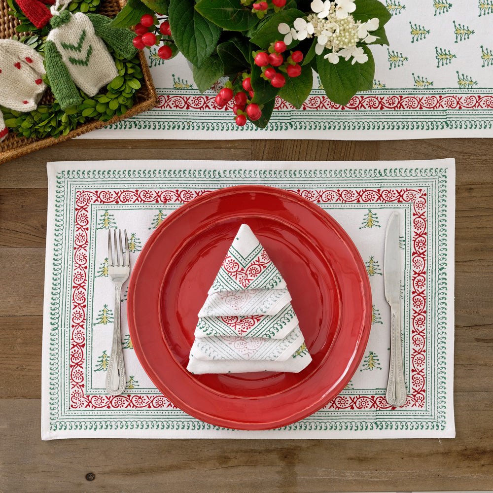 Christmas Tree Print Napkin folded in the shape of a tree on a red plate and matching placemat