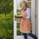 Model wearing Harvest Pinecone Orange & Green Apron carrying stack of plates and chargers