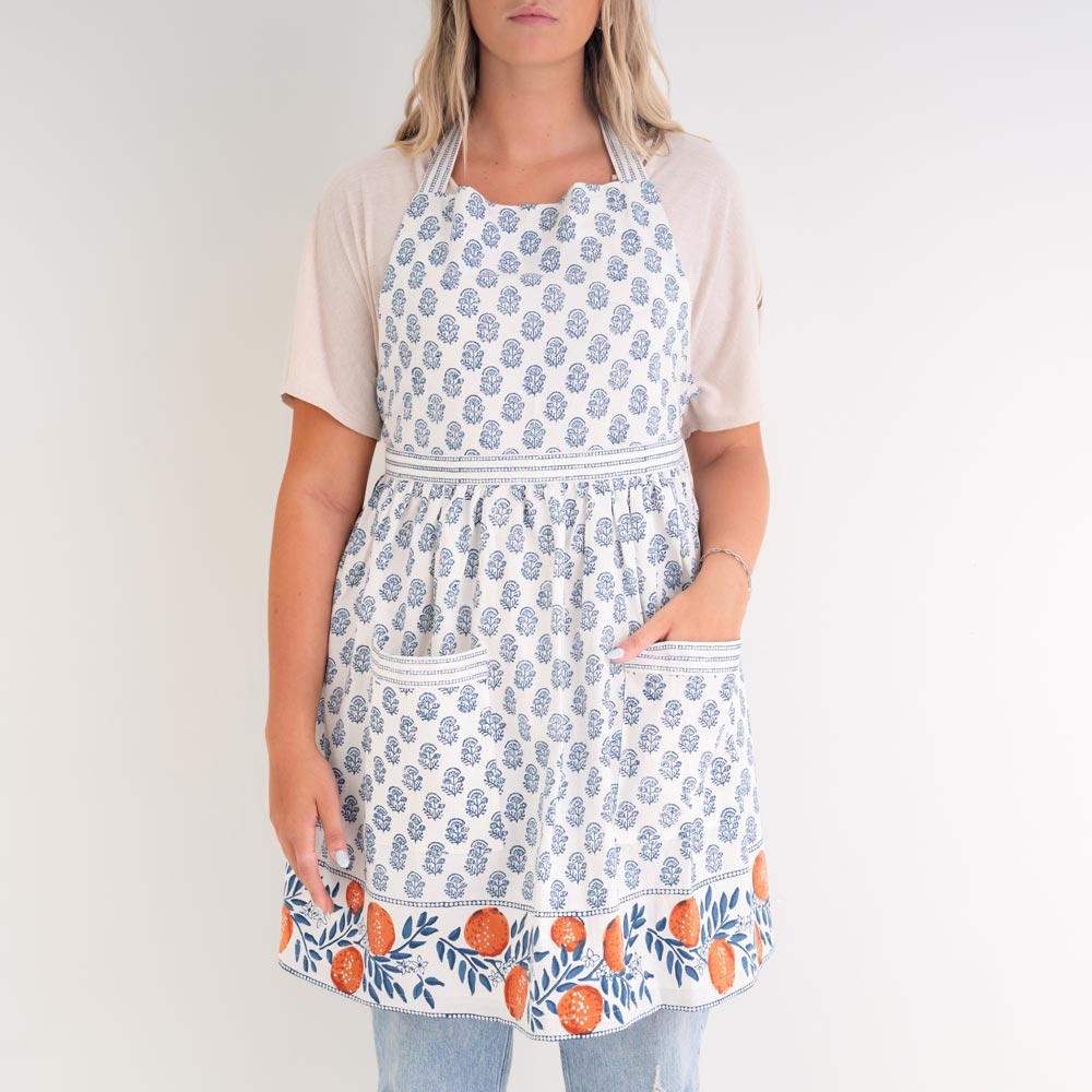 model wearing apron with blue floral print and oranges along border