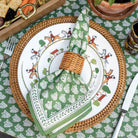 Pom Buti Green napkin with wicker napkin ring on plate and wicker charger on matching tablecloth